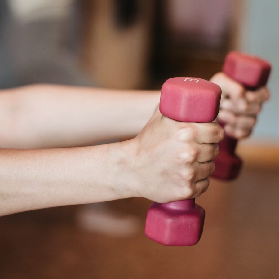 A person holding two pink dumbbells in their hands.