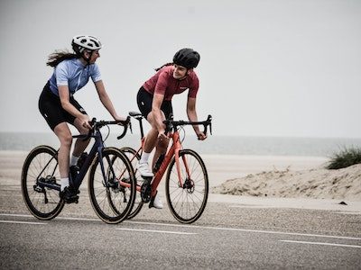 Two people riding bicycles on a road near the ocean.